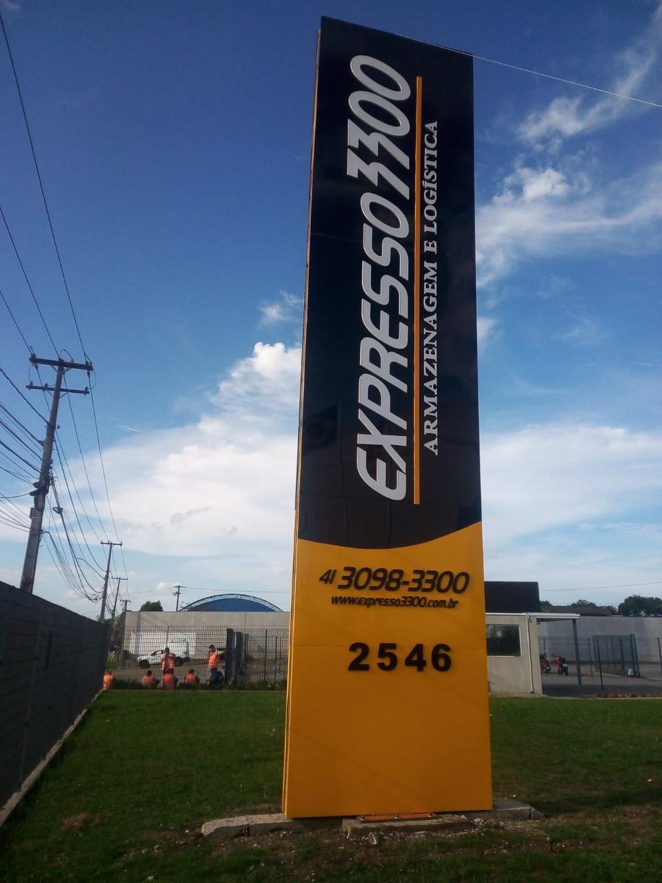Totem alto em ACM preto e amarelo da Expresso 3300 instalado em frente à empresa